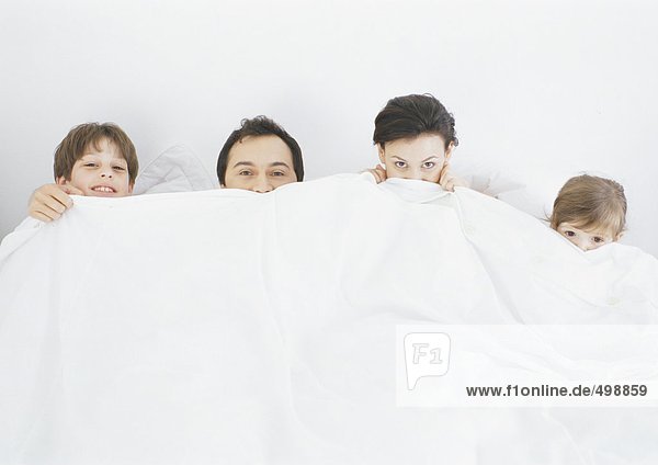 Family in bed pulling covers up under noses