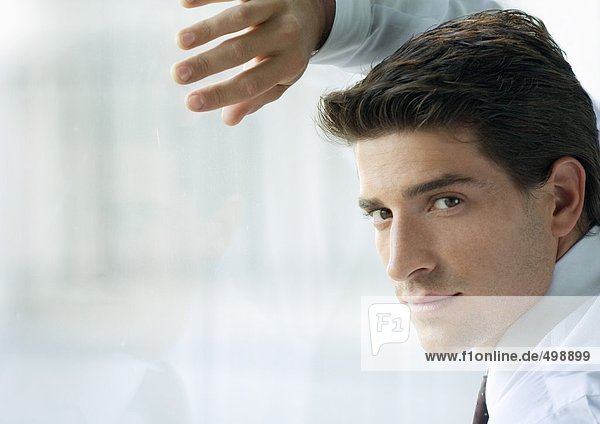Geschäftsmann  lehnt sich gegen das Fenster  schaut über die Schulter zur Kamera