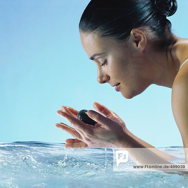Frau im Wasser hält Steine in Händen mit geschlossenen Augen  Seitenansicht