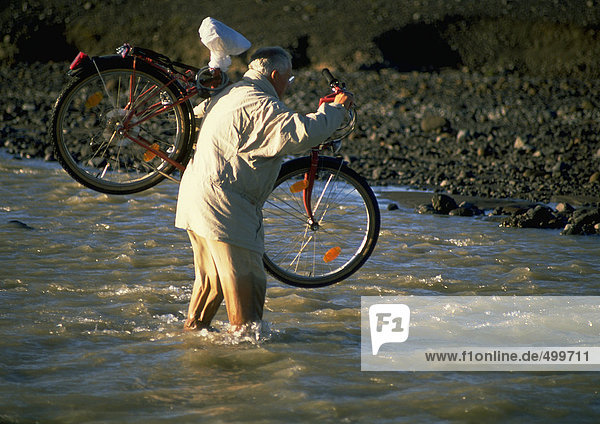 Island  Mann trägt Fahrrad durchs Wasser