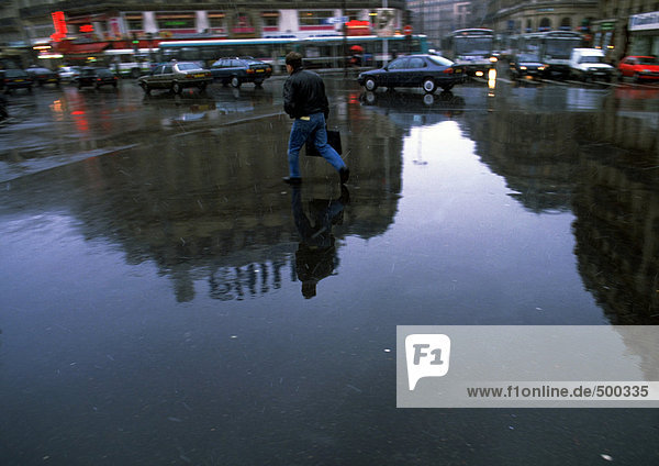 Person walking through square on wet ground with reflection