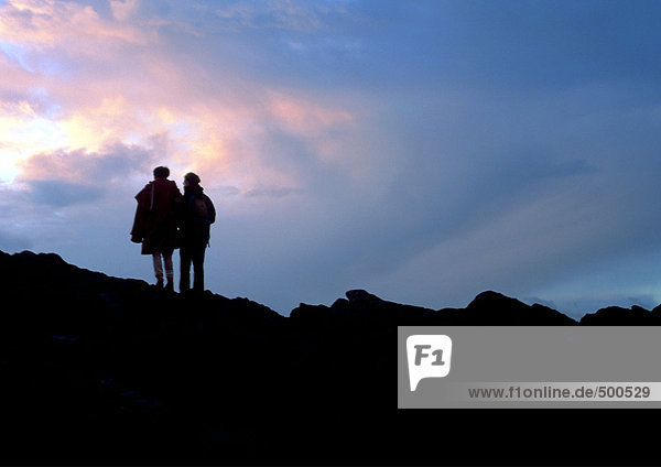 Two people standing on rocky mountain  silhouette