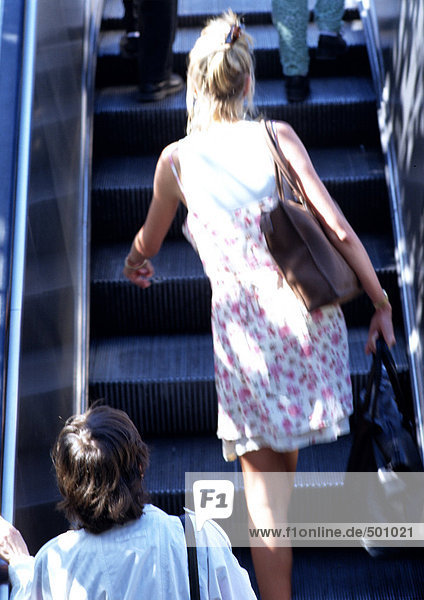 Frau geht die Rolltreppe hoch,  Rückansicht.