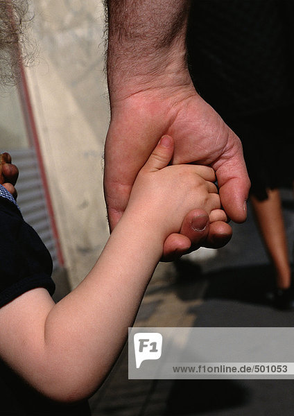 Das Kind hält die Hand des Mannes  ganz nah.