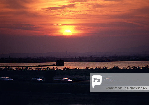 Sonnenuntergang über Wasser und Verkehr auf der Autobahn