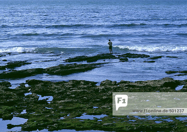 Person beim Fischen auf Felsen in der Nähe von brechenden Wellen