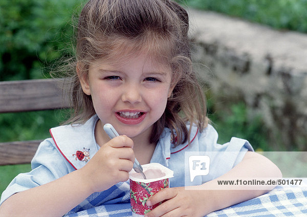 Ein junges Mädchen isst draußen Joghurt.