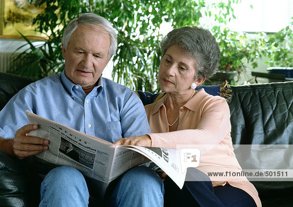 Ein älteres Paar auf der Couch  das Zeitung liest.