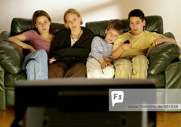 Fokus auf junge Erwachsene und Kinder  die im Hintergrund auf der Couch sitzen  Rückansicht des Fernsehers im Vordergrund  verschwommen.