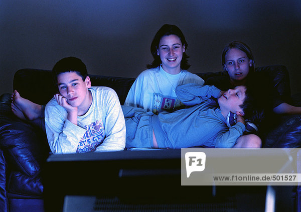 Young adults sitting together on couch watching television in the dark.