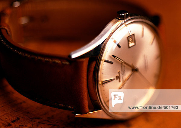 Armbanduhr mit weißem Zifferblatt und Lederband  Holzuntergrund  Nahaufnahme