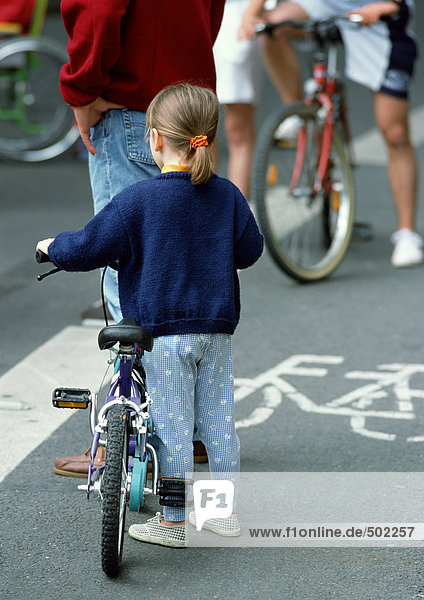 Little girl standing beside bicycle in bikelane  rear view