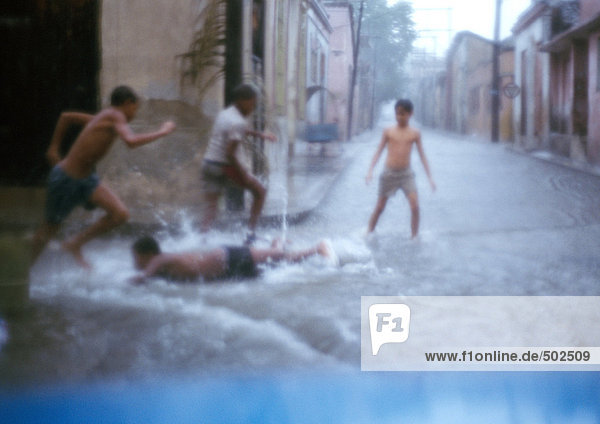 Jungen rennen in einer wassergesättigten Straße  einer liegt auf dem Boden  verschwommen.