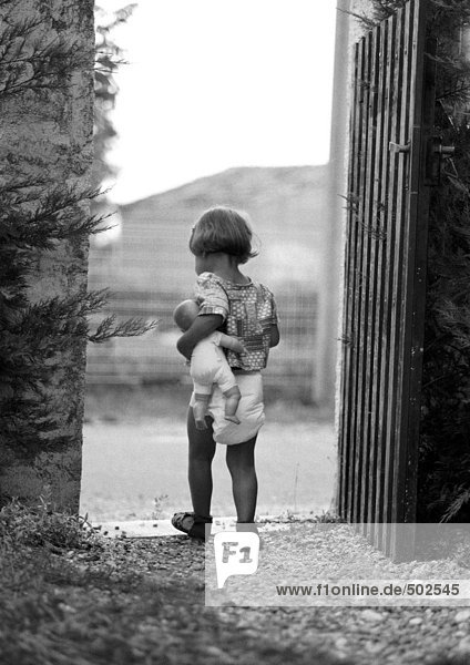 Kleines Mädchen hält Babypuppe im Tor  Rückansicht  s/w