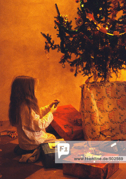 Mädchen kniend vor dem Weihnachtsbaum  Geschenke betrachtend