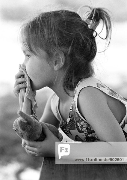 Mädchen hält Plüschtier in der Hand und Stoffstück über dem Mund  Seitenansicht  s/w