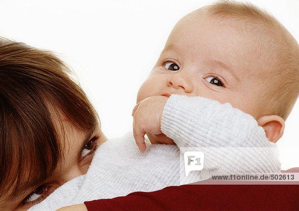 Baby mit der Hand im Mund mit Blick auf die Kamera  Frau  Oberkopf  Blick auf das Baby  Nahaufnahme