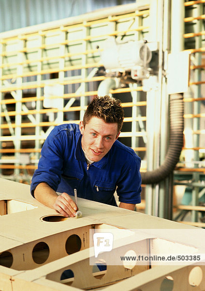 Mann im Overall hinter Holzarbeiten  Blick in Kamera  Kopf und Schultern