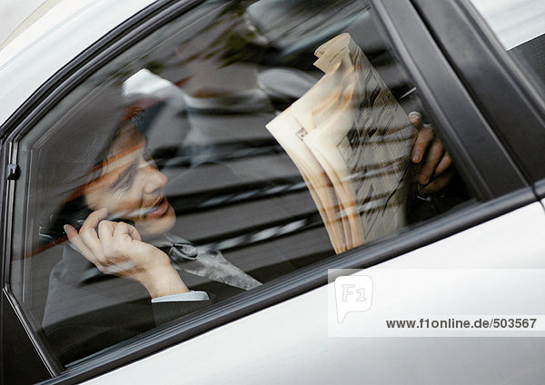 Geschäftsmann sitzt hinten im Auto  hält Zeitung und Handy  durchs Fenster gesehen