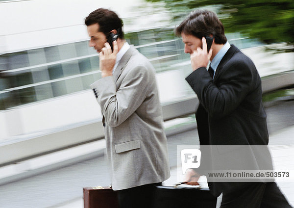 Two businessmen holding briefcase and cell phone  walking outside