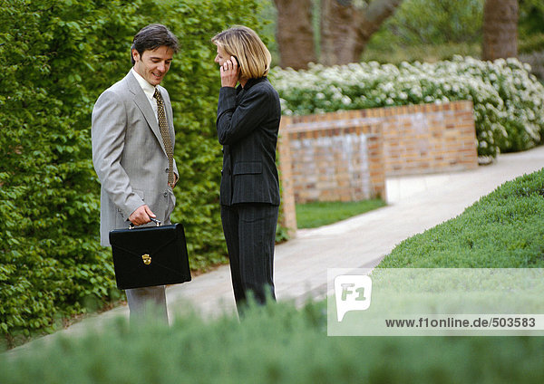 Businessman and businesswoman standing in park  businesswoman using cell phone