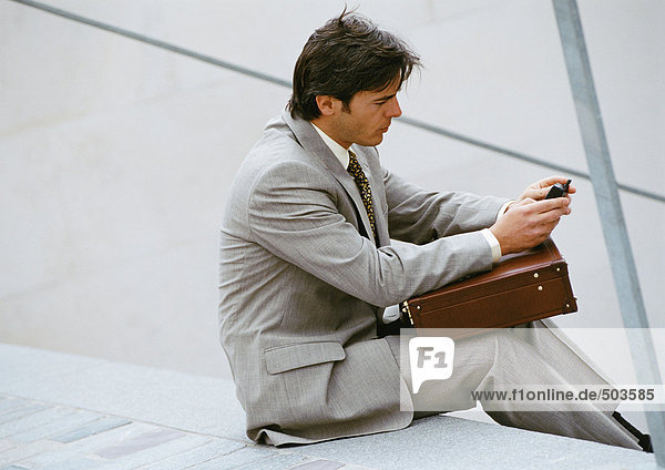 Geschäftsmann sitzt auf einer Treppe und schaut auf sein Handy.