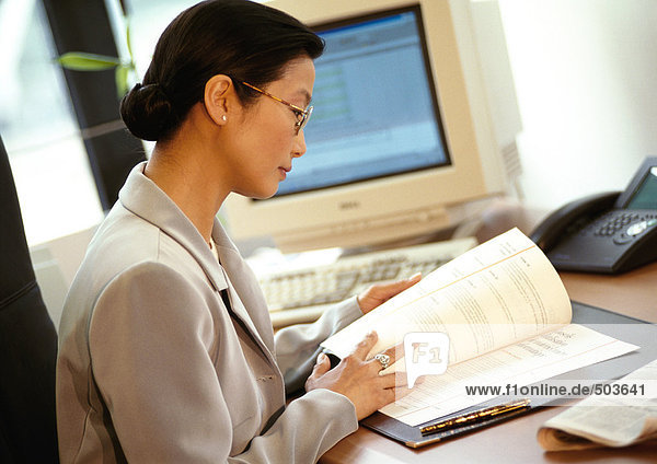 Businesswoman sitting at desk  reading document  side view