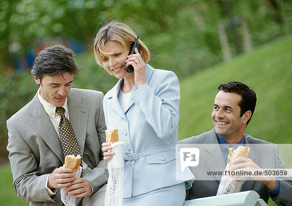 Drei Geschäftsleute mit Sandwiches im Freien  einer mit Handy