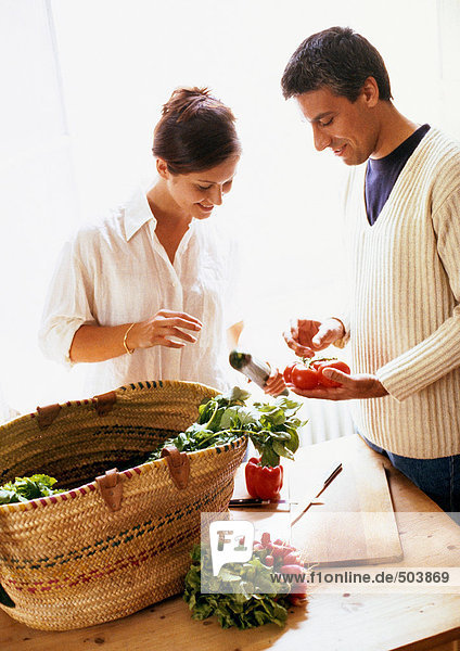 Frau und Mann stehen hinter dem Marktkorb und schauen sich Gemüse an.