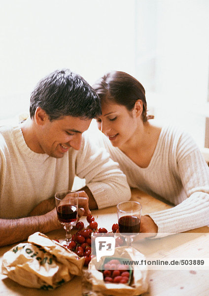 Paar am Tisch sitzend  Kopf und Schultern  mit Beeren  Kirschen und Gläsern Rotwein
