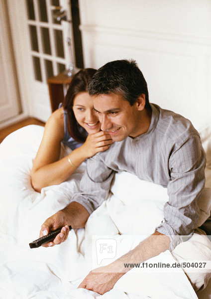 Paar auf dem Bett sitzend  Mann mit Fernbedienung