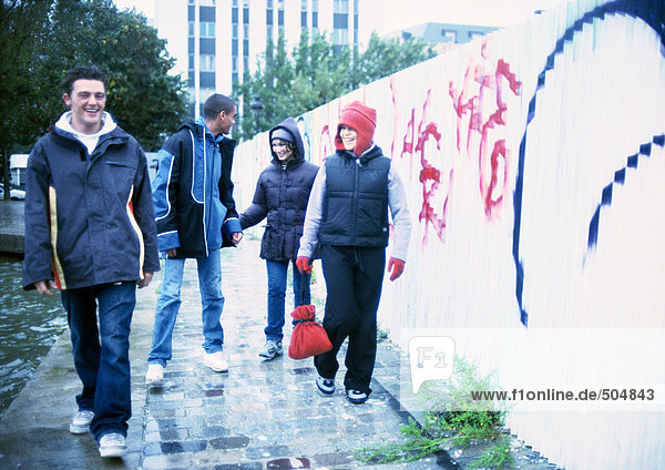 Vier junge Leute  die auf dem Bürgersteig neben der mit Graffiti bedeckten Wand laufen