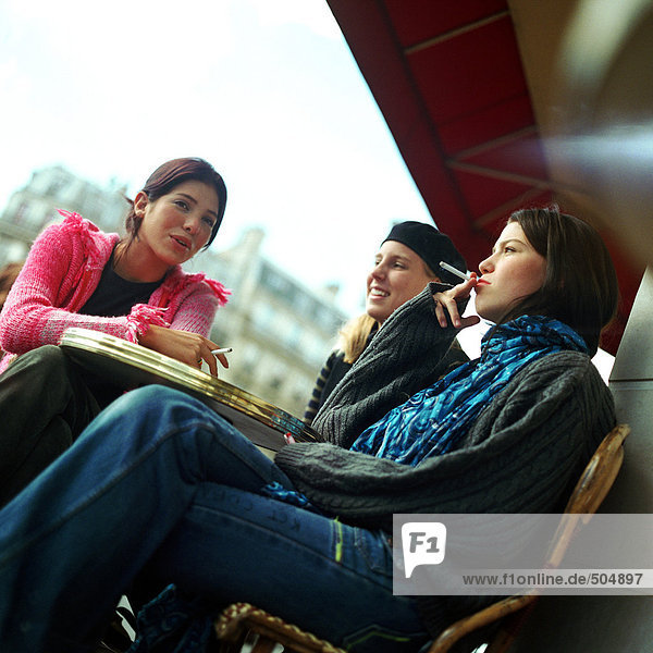 Three teenage girls sitting at cafe terrace  smoking cigarettes  low angle view