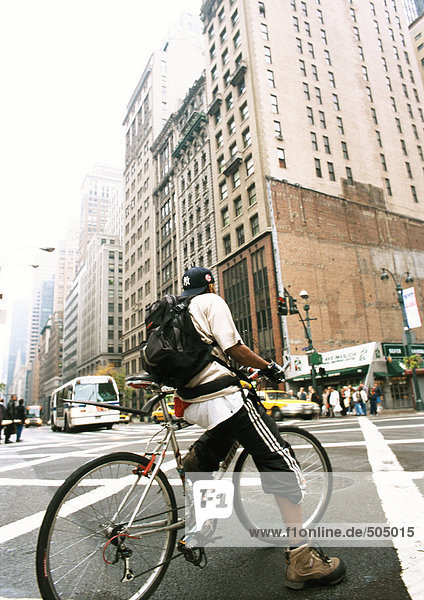 Man riding bike in street  buildings in background