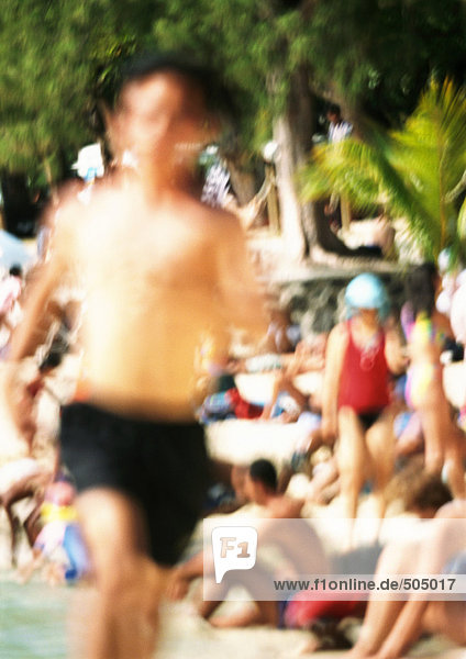Bare-chested person running  people in background on beach  blurred