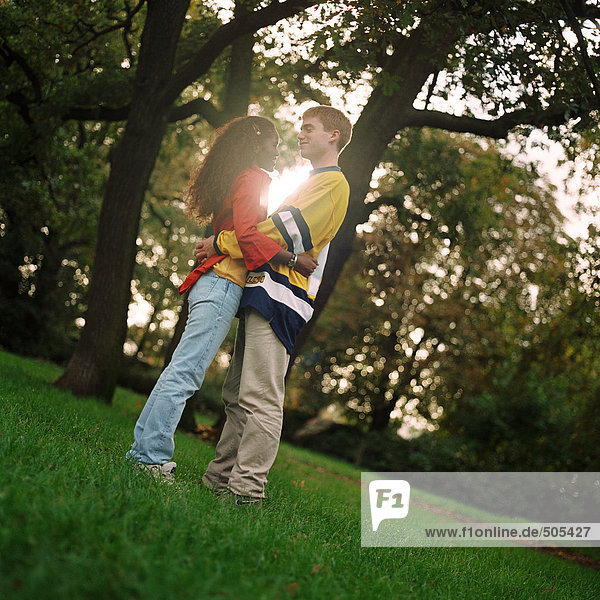 Young man and woman standing on grass  embracing  side view  full length