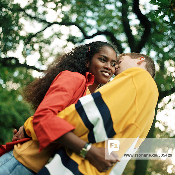 Young couple embracing outdoors  man whispering into young woman's ear  low angle view
