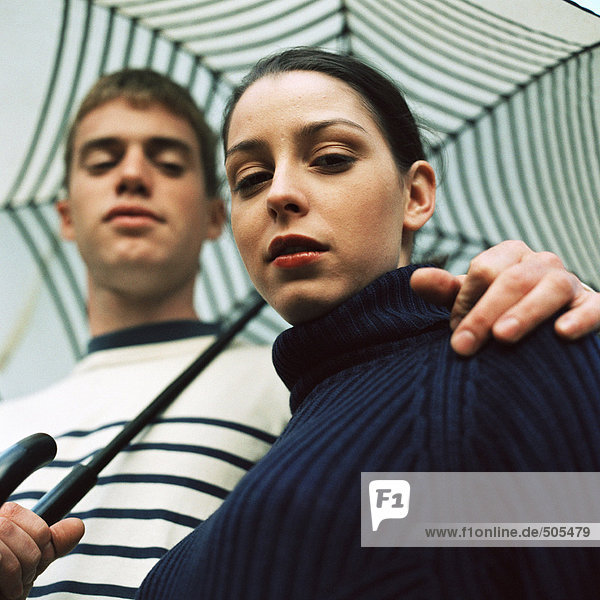 Young man and young woman under umbrella outside  man's hand on woman's shoulder