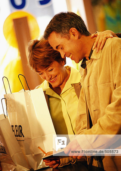 Mann und Frau mit Einkaufstaschen  Bezahlung mit Scheck  Taille oben