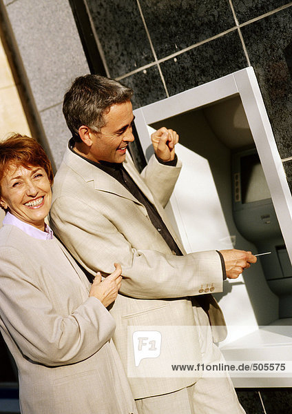 Mann und Frau in Jacken am Geldautomaten  lächelnd