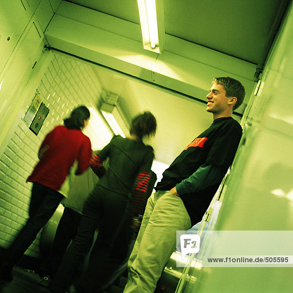 Young man standing in subway corridor  side view  people walking  rear view in background