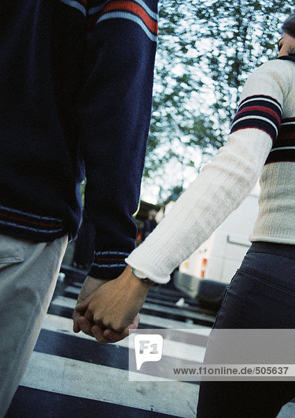 Young couple holding hands at pedestrian crossing  close up  rear view