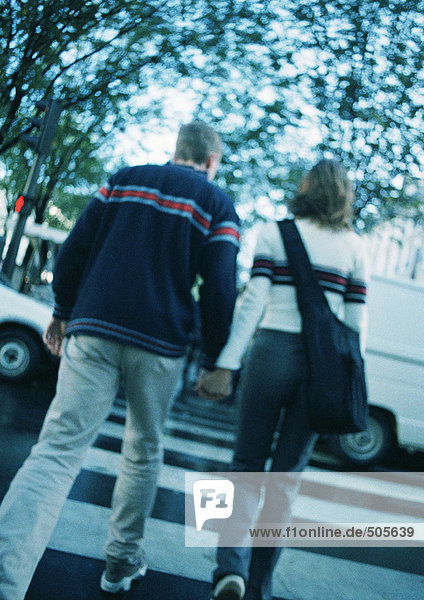 Young couple holding hands  crossing at pedestrian crossing  blurred  rear view