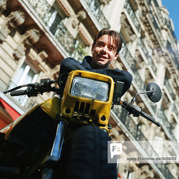 Teenager-Junge auf stationärem Motorrad  lächelnd in die Kamera  Blickwinkel niedrig
