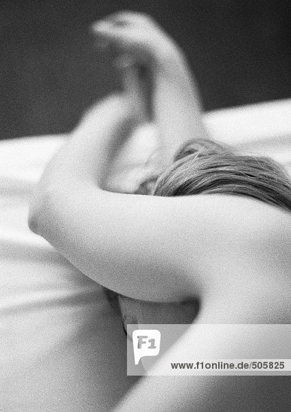 Nackte Frau auf dem Bett liegend mit Armen über dem Kopf  Nahaufnahme  schwarz-weiß.