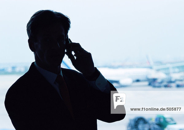 Man wearing suit  holding cell phone to ear  silhouette  airplanes in background.