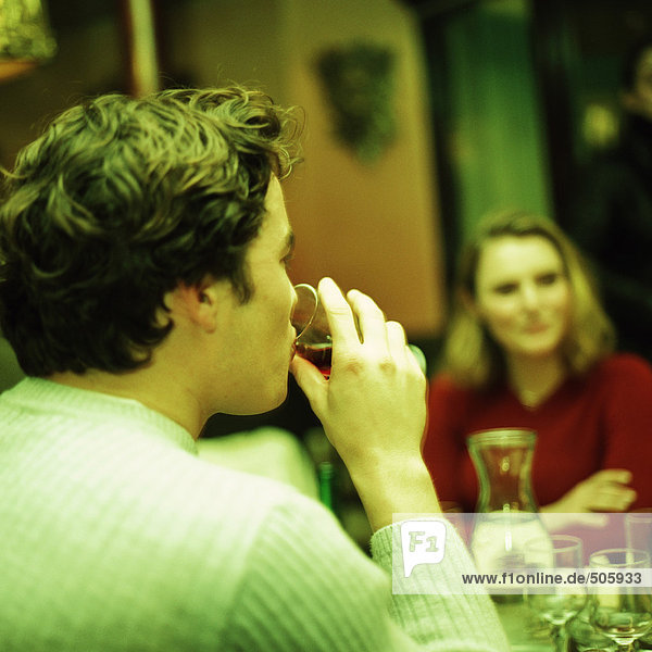 Junge Leute am Tisch  junger Mann im Vordergrund trinkend  Rückansicht