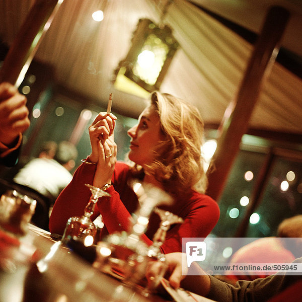 Junge Frau mit Zigarette und Blick über die Schulter auf den Tisch im Restaurant