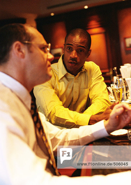 Businessmen sitting at bar talking  side view.