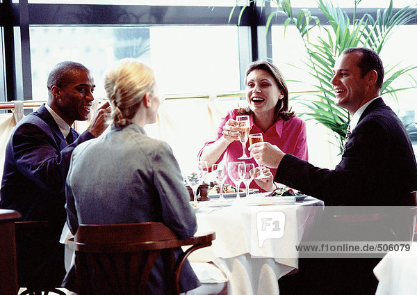 Gruppe von Geschäftsleuten  die zusammen am Tisch sitzen  lächeln und Gläser erheben.